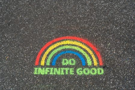 A rainbow chalked onto a pavement with the words 'Do Infinite Good' underneath