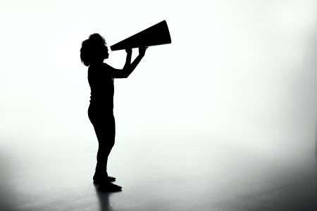 Black shadow outline of a person in front of a white background shouting through a megaphone