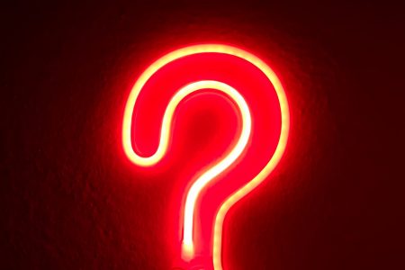 A red neon question mark outline light on a dark background