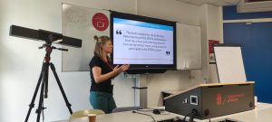 Annemieke stands in front of the screen with a quote from the Dutch teenagers. The quote says that the best moment for the teenager was meeting the SEEDS ambassadors and collecting ideas on how to attract more young people to STEM