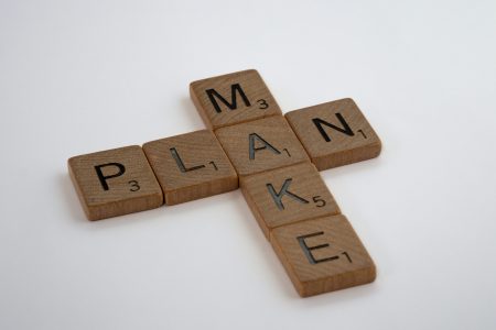 Wooden letters of the game scrabble with 'plan' lying horizontally and 'make' lying vertically, connected through the common a in both words